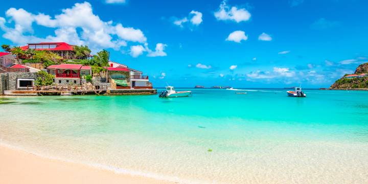 St Martin base showing azure blue waters on a beach with a bright blue sky with a couple boats on the water